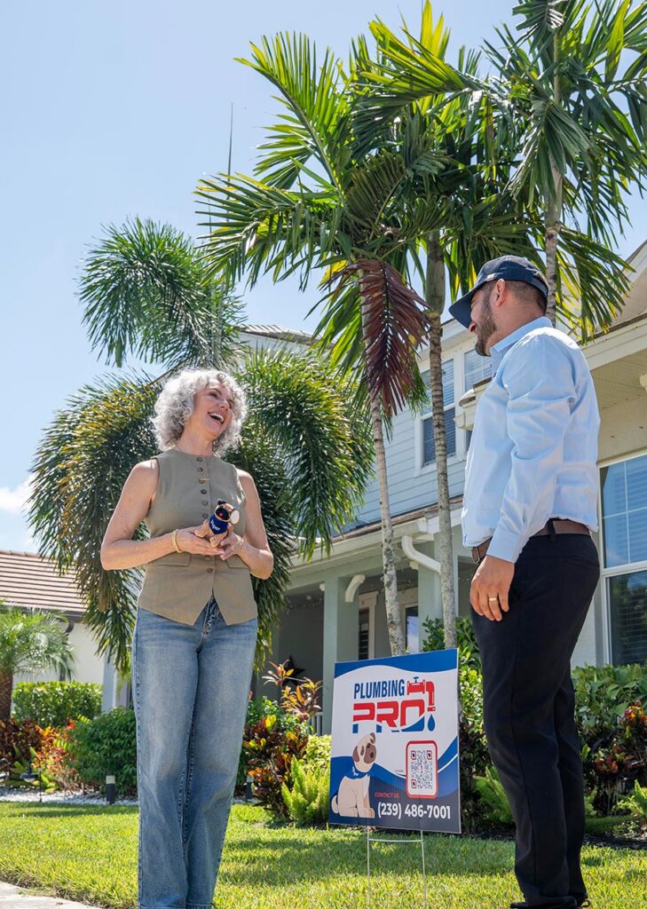 PlumbingPro technician talking with a homeowner beside a PlumbingPro yard sign